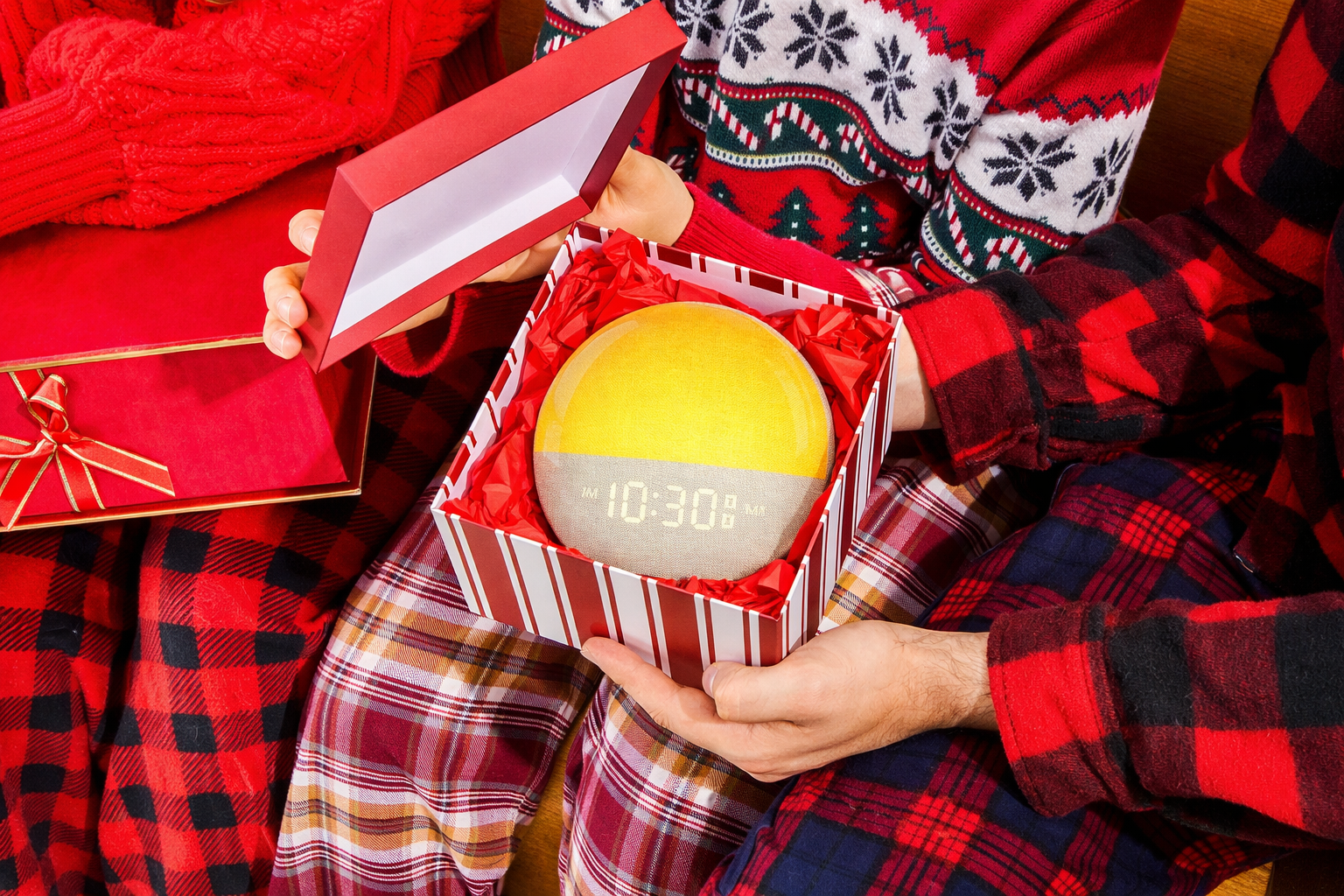 gxfusion sunrise alarm clock banner -Person in festive pajamas holding a gift box with a digital clock inside, surrounded by more gifts.
